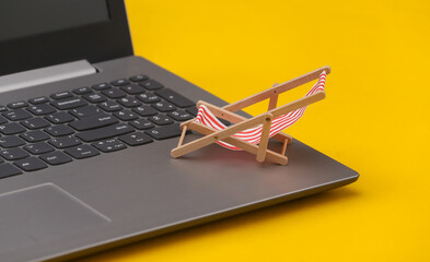Beach chairs on a laptop keyboard. Beach Vacation Concept. Yellow background