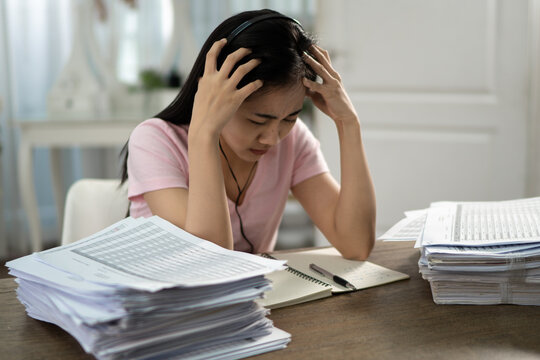 A beautiful Asian woman wearing a pink shirt and headphones is crying over an online class in her home..