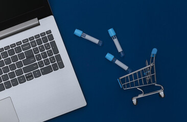 Shopping trolley with test tubes, laptop on classic  blue background. Healthcare. Top view. Flat lay