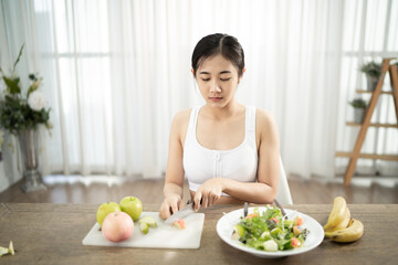 A healthy, healthy Asian woman uses a fruit knife to make a salad to eat inside her home. Healthy weight loss ideas.