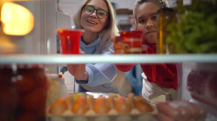 Two diverse girls looking in fridge taking pudding for snack