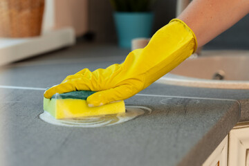 Woman's hands in yellow gloves cleaning counter top in kitchen