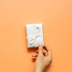 Hand holding silver gift box on orange background. top view, copy space