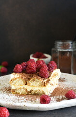 Tiramisu with raspberries on a dark concrete background. The classic Italian dessert is tiramisu.
