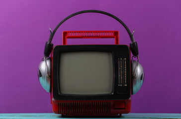 Red retro old portable mini tv set with headphones on purple background.