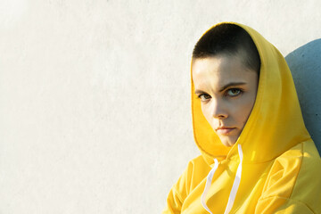 Serious confident strong young woman with short hair in yellow hoodie looking at camera.
