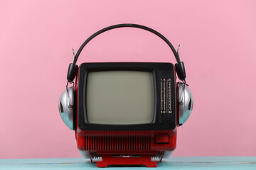 Red retro old portable mini tv set with headphones on pink background.