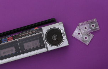 80s Retro outdated portable stereo radio cassette recorder and audio cassette on purple background. Top view. Flat lay