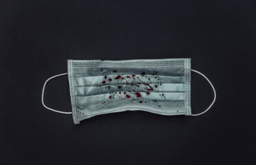 Facial medical mask with blood on a black background. Pandemic covid-19, pneumonia or tuberculosis....