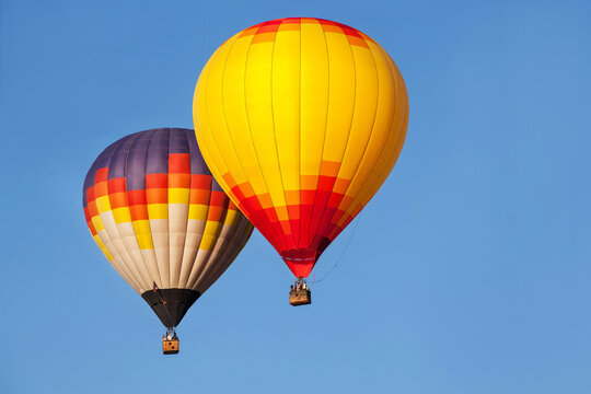 Two multi-colored hot air balloons flying in the blue sky. 
