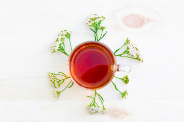 The cup of black herbal tea with branches of yarrow on wooden background. Top view. © Евгений Шемякин