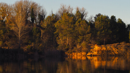 Étang de carrière surmonté d'une petite falaise de calcaire, illuminée par le soleil couchant