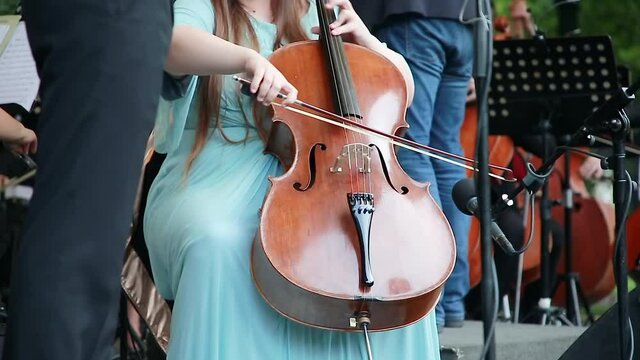 A female musician plays a bow on a cello violin.