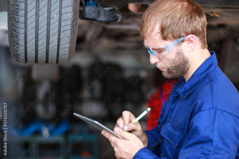 Wall mural A male auto mechanic in uniform is examining a tire while working in auto service