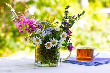 Bouquet of medicinal fresh herbs and a cup of herbal tea on natural background.