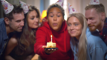 Excited girl ready to blow out candles on cake on birthday party with happy friends.