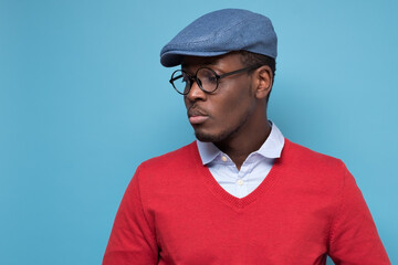 Handsome african young man in blue cao and glasses thinking looking aside.