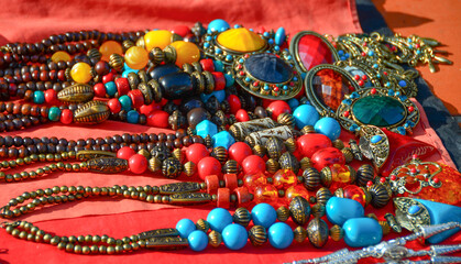 The necklace is carved from ivory, carved brass, round, with stones, stones, many colorful, handmade, tied in a beautiful necklace, arranged on a red cloth.