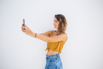 Stylish beautiful lady in casual outfit capturing selfie picture by smartphone on gray background