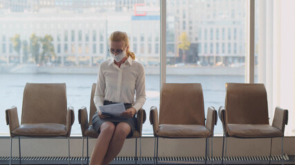 Elegant mature lady putting on facial mask sitting in office corridor waiting for meeting with employer