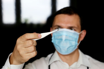 Coronavirus symptoms, man in medical mask measures body temperature. Doctor with digital...