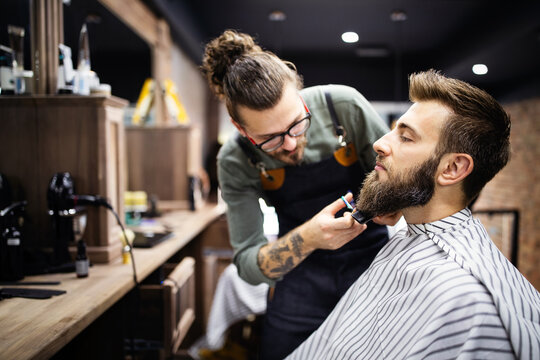 Happy young handsome man visiting hairstylist in barber shop salon