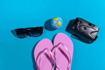 Travel concept. Camera, globe, sunglasses, flip flops on blue background with shadow. Top view