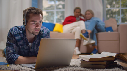 Young man in heaphones having educational webinar on compute lying on floor in dorm living room