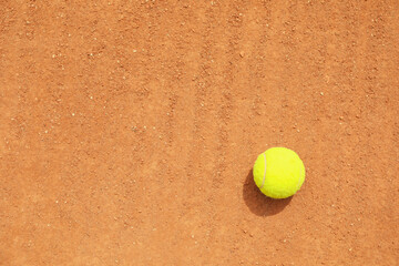 Light green tennis ball on clay court, space for text