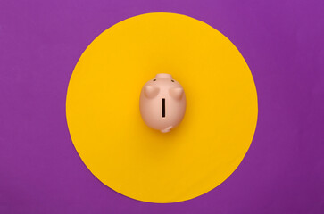 Piggy bank on purple background with yellow circle. Conceptual studio shot. Minimalism. Top view