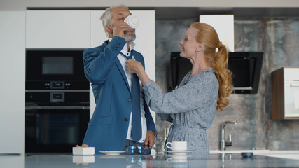 Senior woman help husband with tie indoors at home kitchen