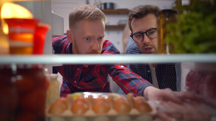 View inside fridge of two guys taking sausages from refrigerator
