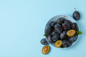 Bowl with plums on blue background, top view