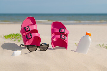 Pink sandals, sunglasses and sunscreen at the beach on a beautiful sunny day. Slippers in the sand...