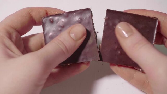 Girl's hands hold bar of chocolate with nuts then break it into several parts. White background and up view.