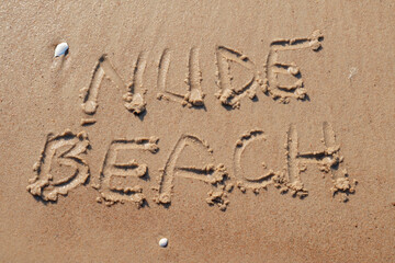 Nude beach letters written on the sand at the beach on a sunny day. Naked sunbathing. Naturalist lifestyle.