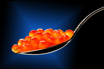 Salmon caviar on a spoon on a dark background with a blue star. Art photo