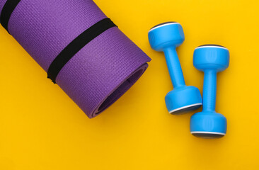 Fitness mat and dumbbells on a yellow background. Healthy lifestyle, fitness training. Top view