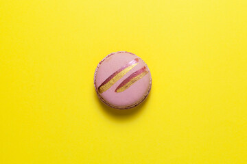 One pink macaron or macaroon with shiny golden stripes lies on a yellow background. Top view, copy space