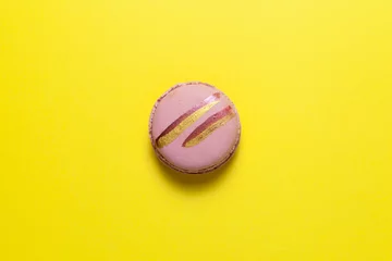 Foto op Canvas One pink macaron or macaroon with shiny golden stripes lies on a yellow background. Top view, copy space © AB-7272