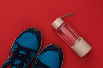 Water bottle and sneakers on red background. Healthy lifestyle, fitness training. Top view