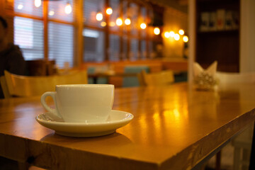 Cup of coffee stands on a wooden table in a restaurant. Blurred cafe background. Warm evening light
