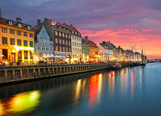 Rows of bars, cafes and restaurants along the Nyhavn Canal illuminated at dusk in Copenhagen
