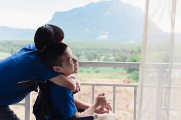 Father hug Asian special child on wheelchair, Boy smiling happy face on balcony house background mountain view, Lifestyle in the education age of disabled children, Happy disability kid concept.