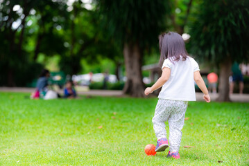 Girl kicked small orange ball with her left foot on vacation in park. Cute child girl exercise with...
