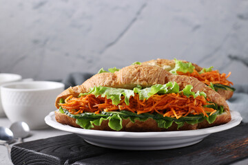 Two vegetarian croissants-sandwiches with lettuce, carrots, cucumbers and two cups of coffee on a light grey concrete background. Breakfast or lunch concept. Closeup