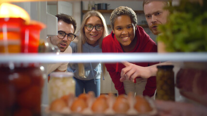Multiethnic friends opening fridge and taking ingredients cooking dinner together in kitchen