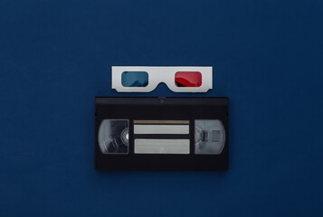Anaglyph 3D glasses and video cassette on classic blue background. Retro media. Color 2020. Tiop view