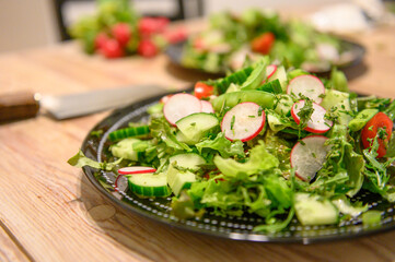 Healthy garden salad with cucumbers, tomatoes, radishes and wild herbs on a black plate standing on a wooden table