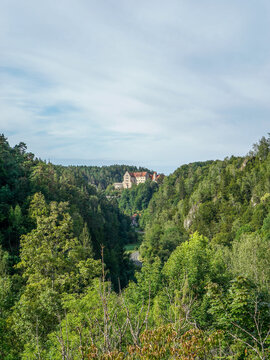 Straße am Bildrand führt zur Burg Rabenstein in der Fränkischen Schweiz bei Tag. Wald aus Nadelbäumen mit einer Burg als Motiv bei blauem Himmel und Tageslicht. Bayern, Deutschland.